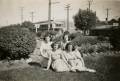 Kath, Bette, Jo and Barb seated on grassed traffic island in front of family home